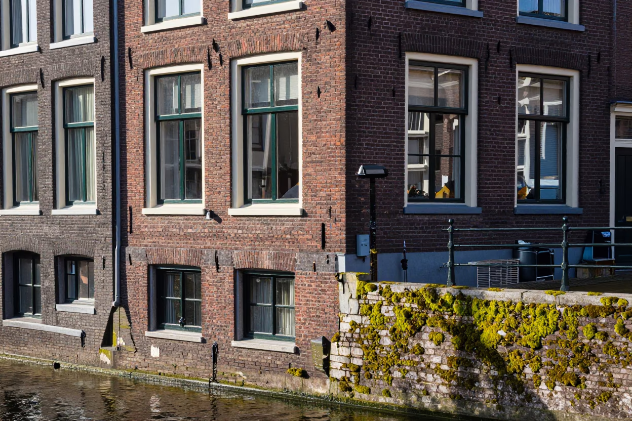 Amsterdam Canal Street Scene with Brick Facades and Mossy Stone Wall at Midday in in Amsterdam, Netherlands