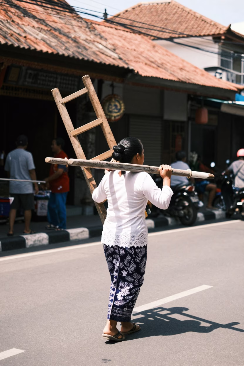 Balinese Woman Carrying Ladder Back Chair Through Denpasar Street Midday Sun in in Denpasar, Indonesia