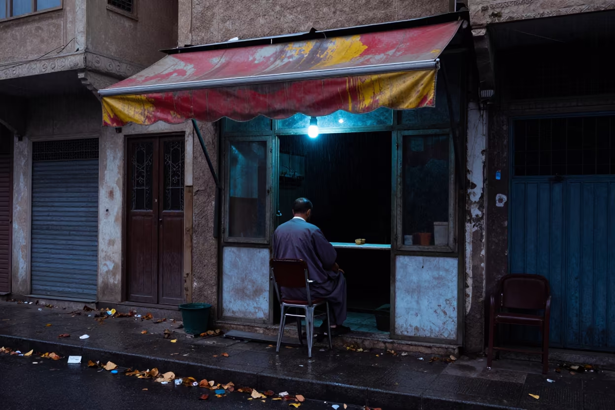 Basra Street Barber Evening Shadow Rim Light in by a rain-darkened kiosk in Basra