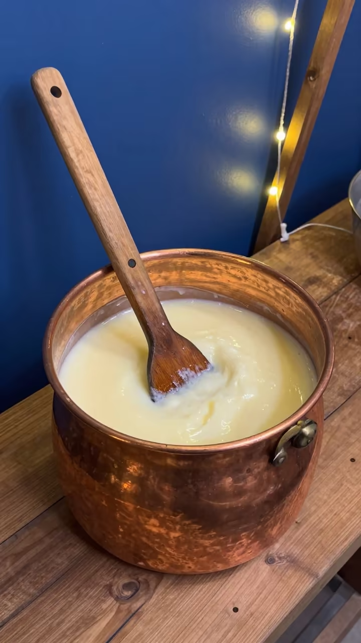 Cheesemaker Stirring Copper Vat Curds in on a wooden workbench in Mumbai