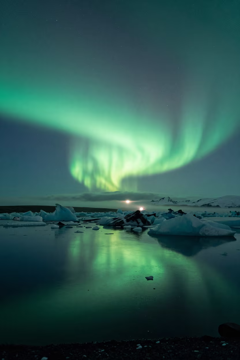 Green Aurora Reflects in Norwegian Glacial Lagoon in beneath a moon-washed horizon in Norway