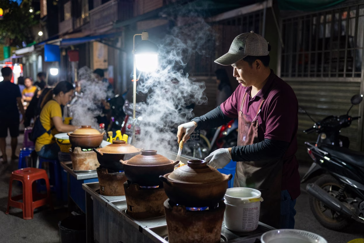 Hanoi Night Street Vendor Cooking Scene with Clay Pots and Metal Stools in in Hanoi, Vietnam