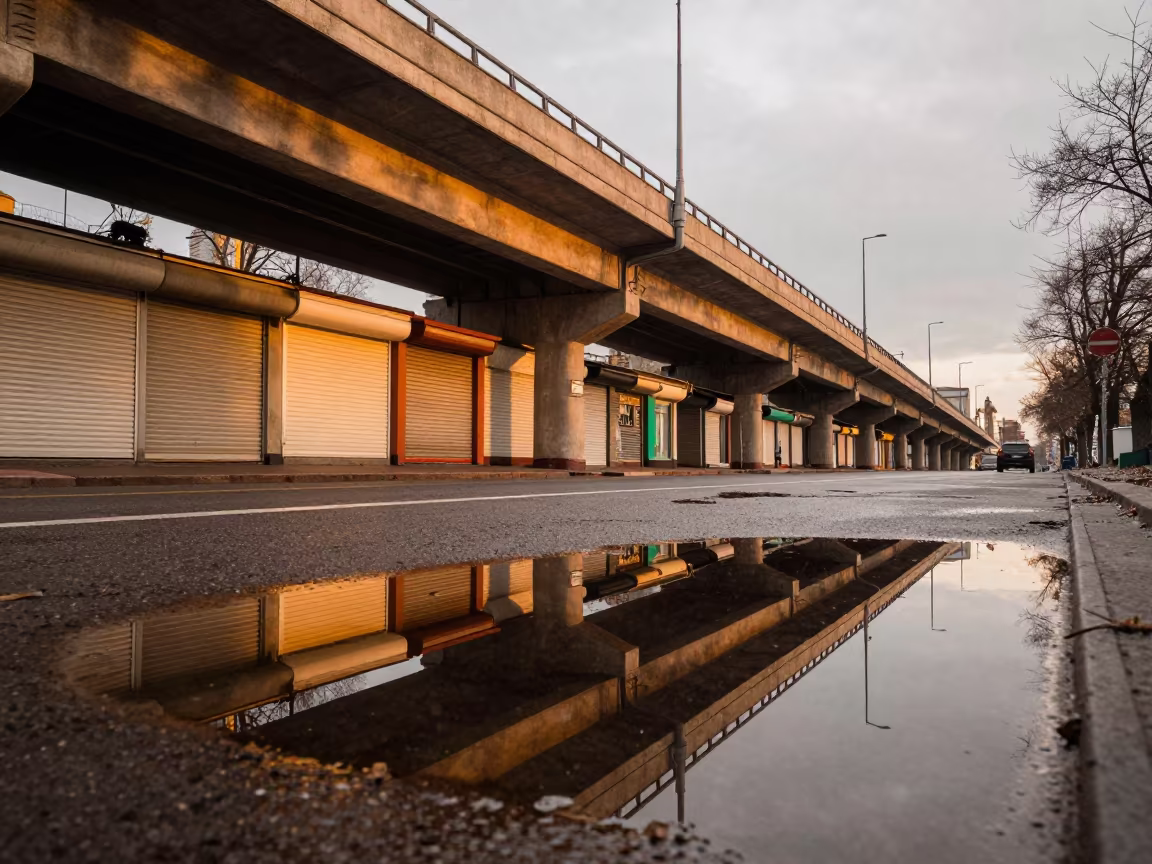Kyiv Puddle Reflects Overpass in Evening Light in along a shuttered arcade in Kyiv