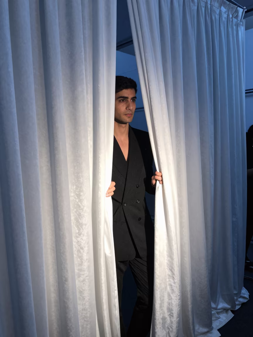 Model Steps Through Curtain Into Blue Hour Light in in a backstage changing corridor in Faisalabad