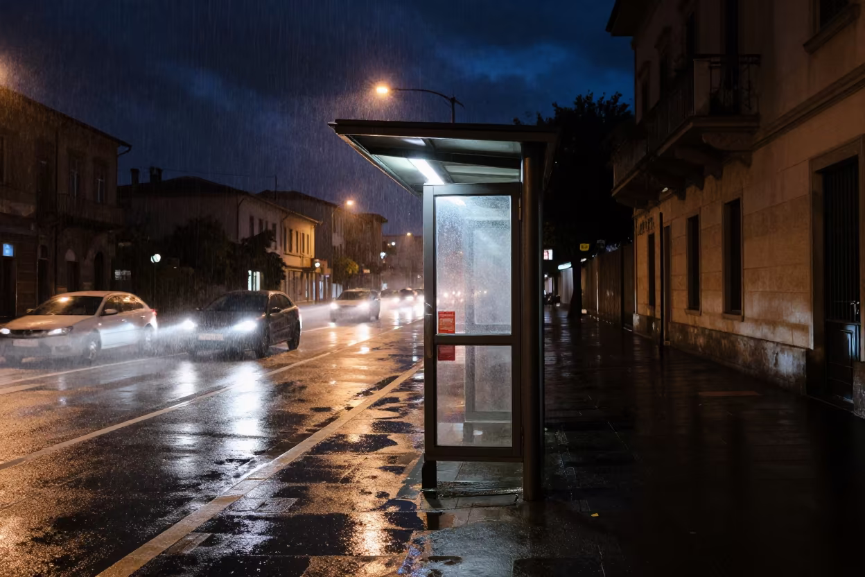 Night Kiosk Under Headlight Wash in Drizzle in beside a steamed-up bus shelter in Rimini