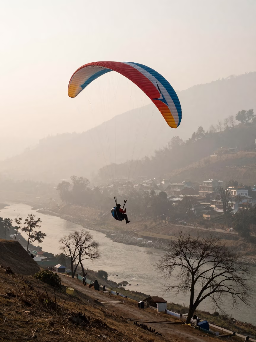 Paraglider Circling Ridge in Winter Mist in by a riverbank near Pokhara