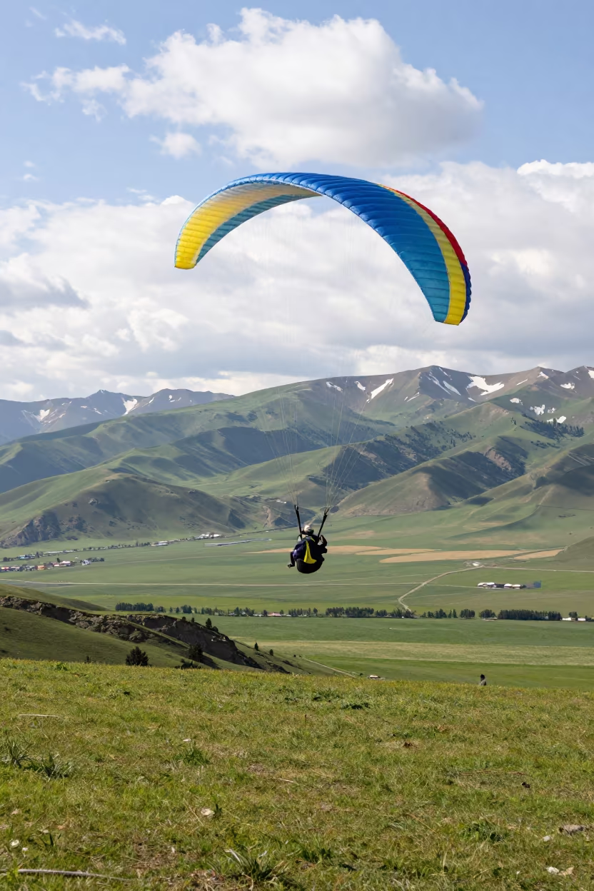 Paraglider Soaring Above Green Valley Fields in near open fields near Bishkek