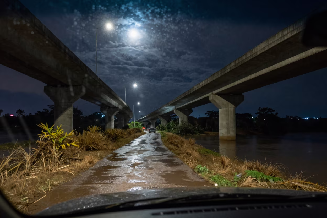 Rain streaked windshield view overpass night Iquitos in along a levee path above floodwater near Iquitos