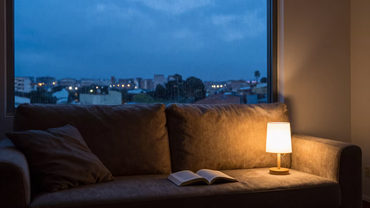 Rainy Evening Sofa With Novel and Lamp in beside a rain-streaked window in Lubango