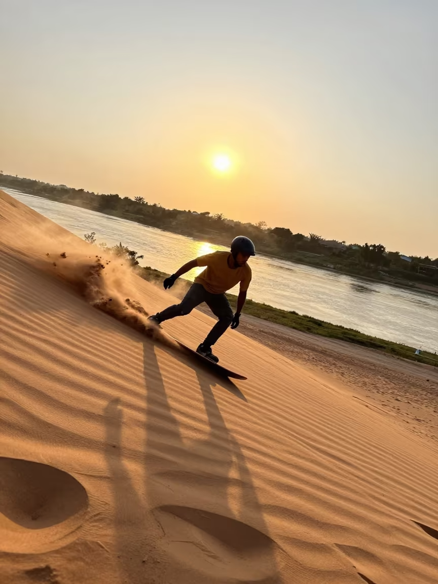 Sandboarder Carving Dune Face at Sunset in by a riverbank near Labé