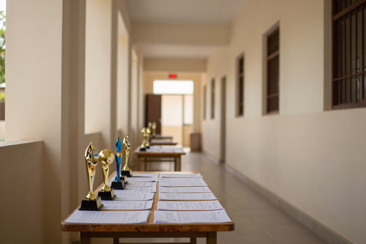 Science Fair Trophies Reflect Exit Sign in Nyala Corridor in at a seminar table covered in notes in Nyala