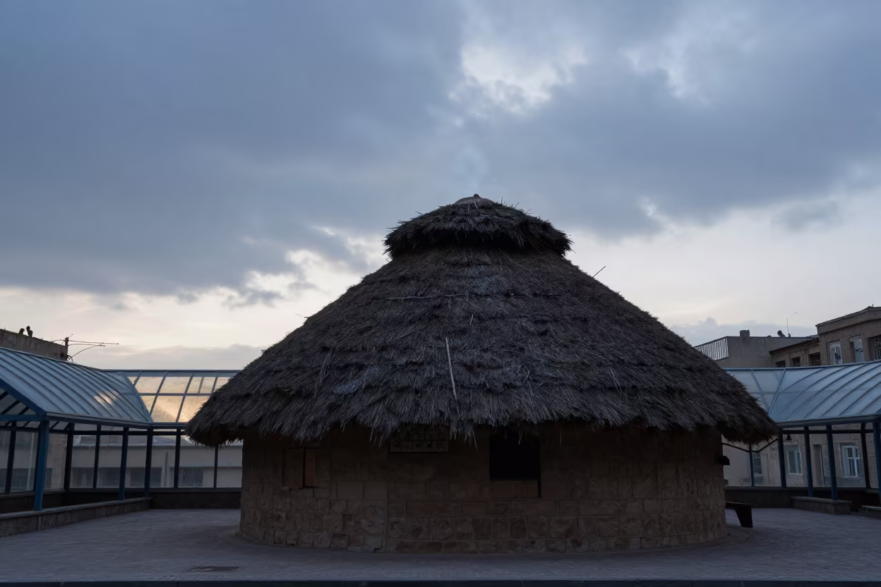 Silhouetted Thatched Longhouse Under Glass Arcade in inside a glass-roofed arcade near Mosul