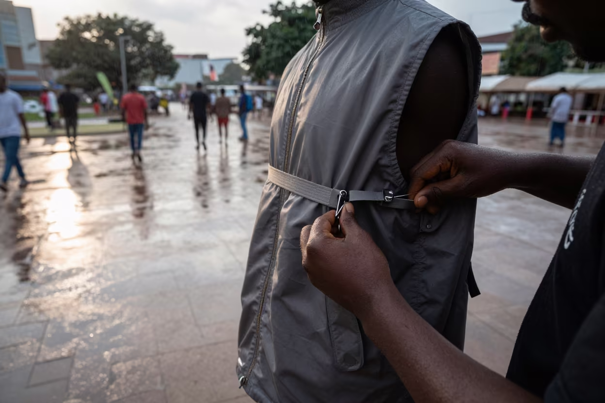 Stylist Adjusts Nylon Vest Straps in Morning Drizzle in across a reflective public plaza near Uyo