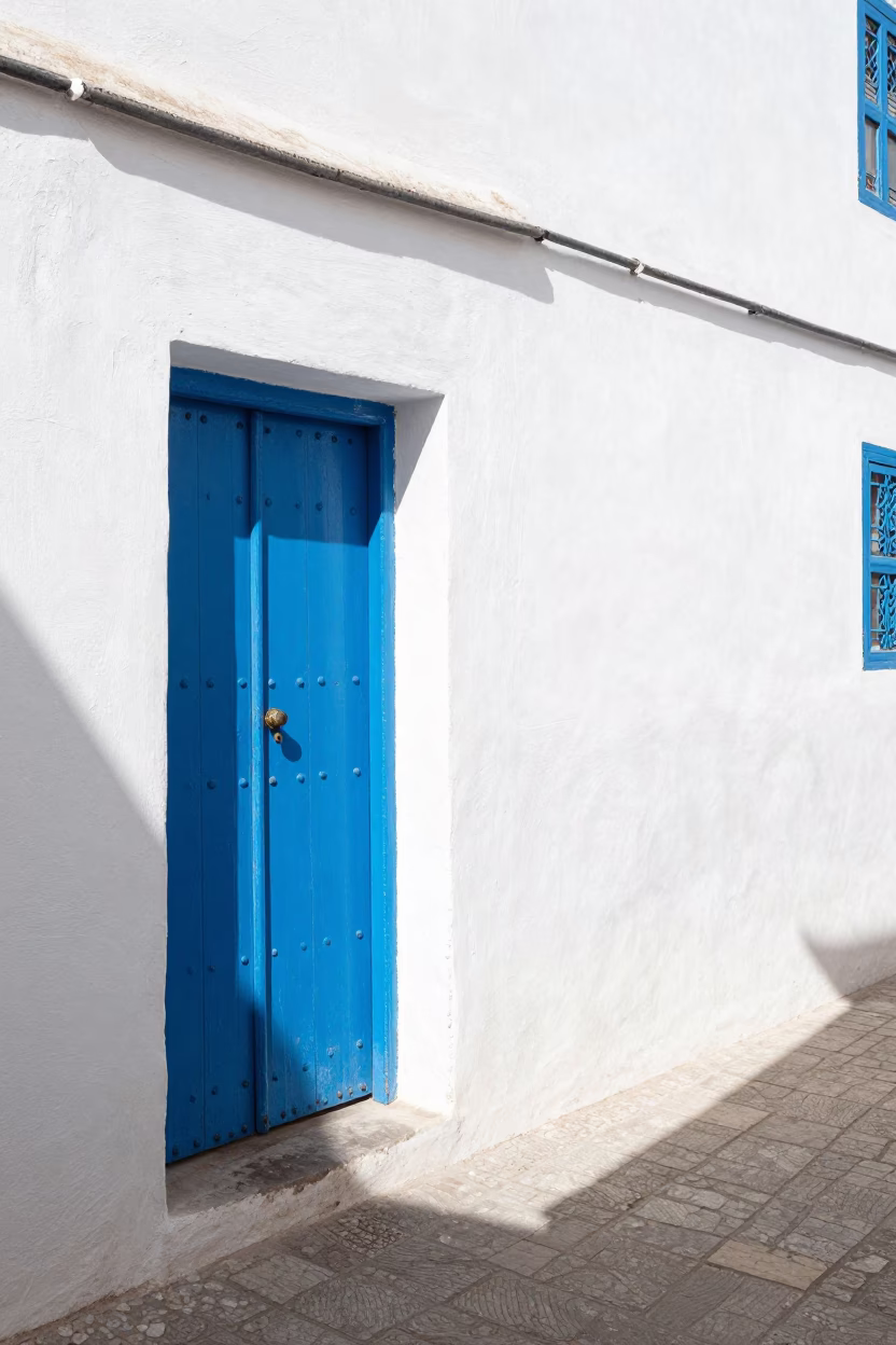 Sunlit Essaouira Medina Alley with White Walls Blue Door and Local Life in Midmorning in in Essaouira, Morocco