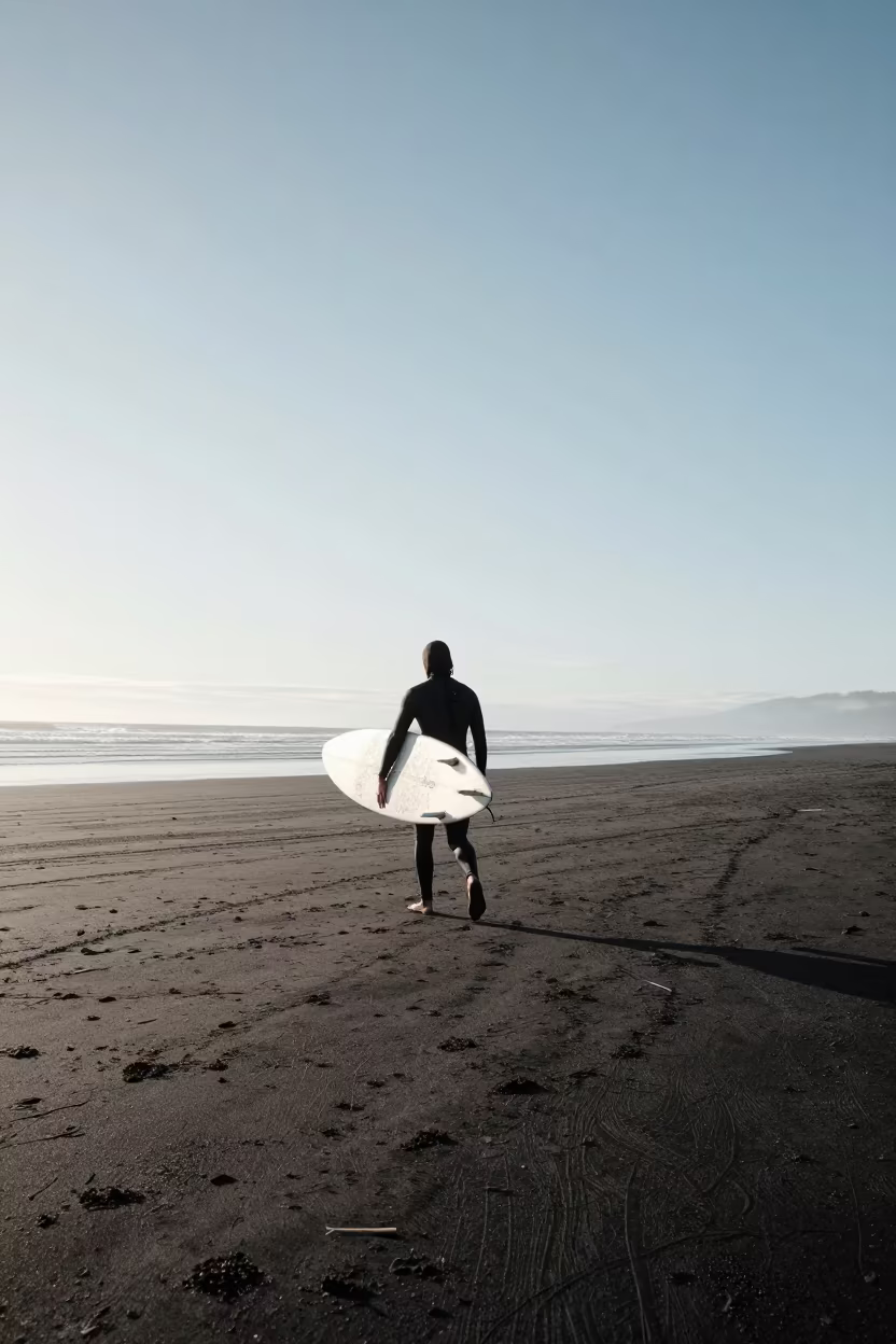 Surfer Carries Longboard Across Black Sand in in British Columbia