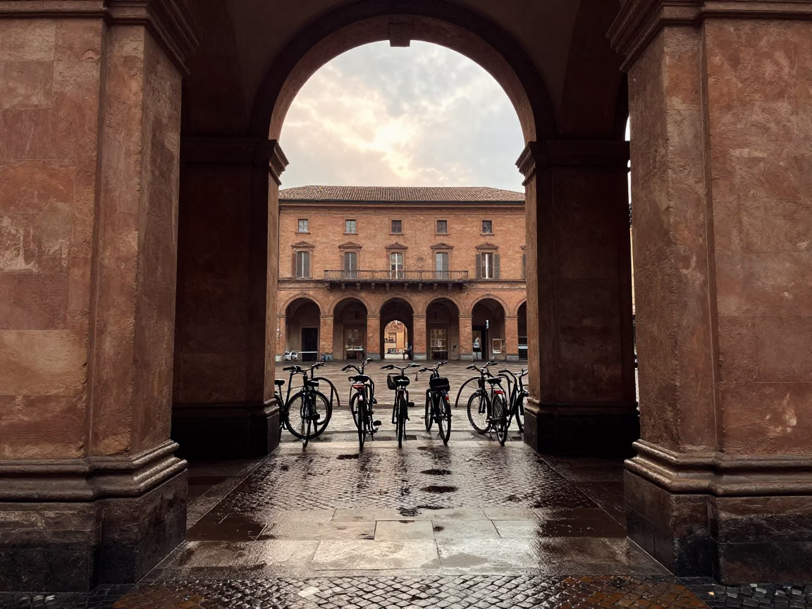 University archway framing wet bicycle rack in Bologna early afternoon with hydrangeas in in Bologna, Italy