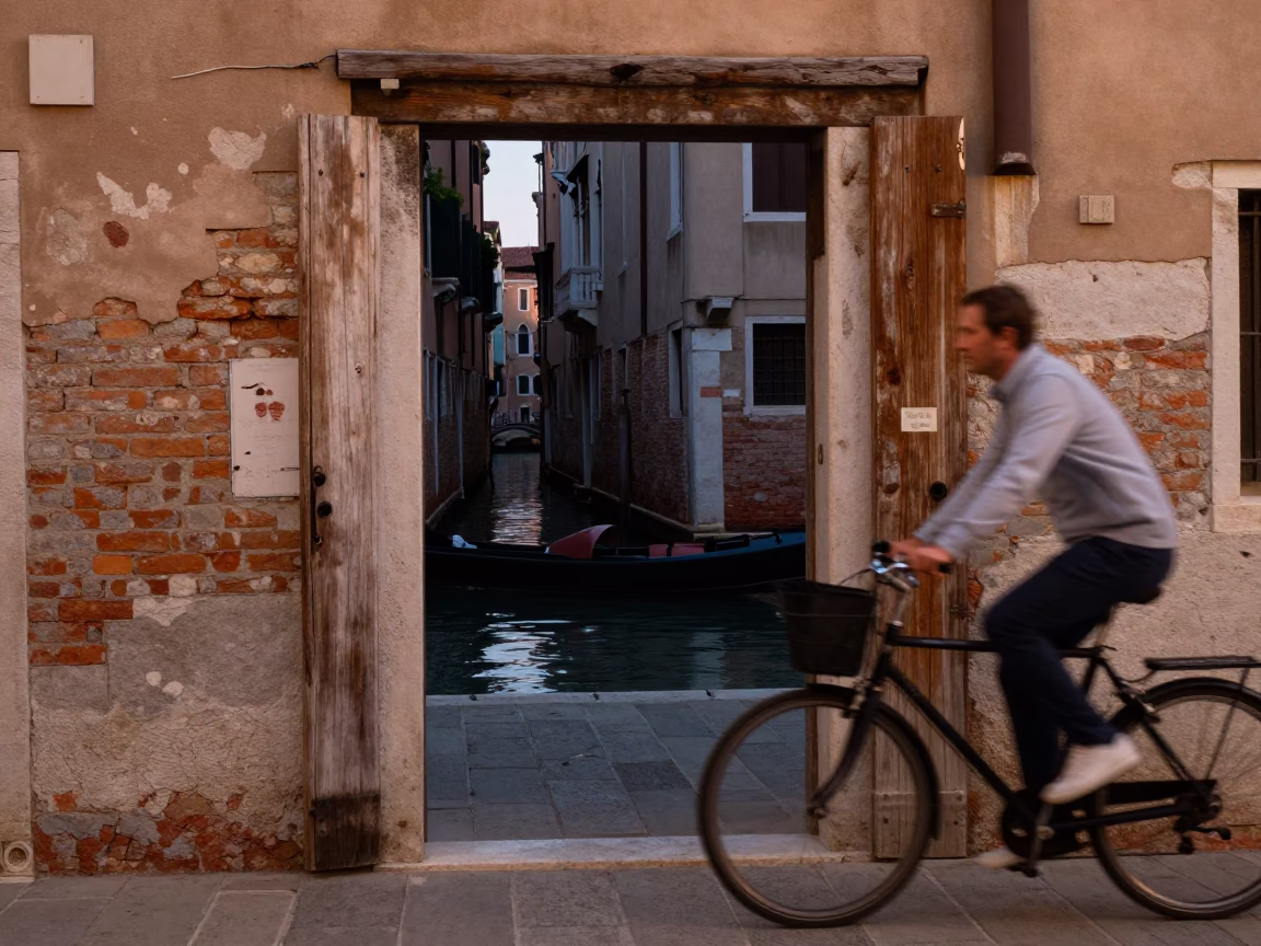 Venice canal side with cyclist passing wooden doorframe and iron hook in in Venice, Italy
