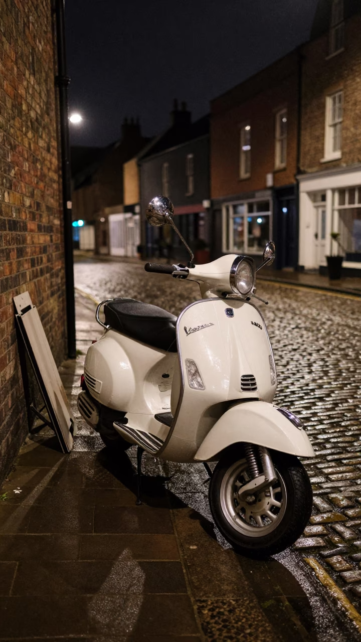 Vintage Vespa parked on Bristol cobblestone lane at night with streetlamp glow in in Bristol, United Kingdom